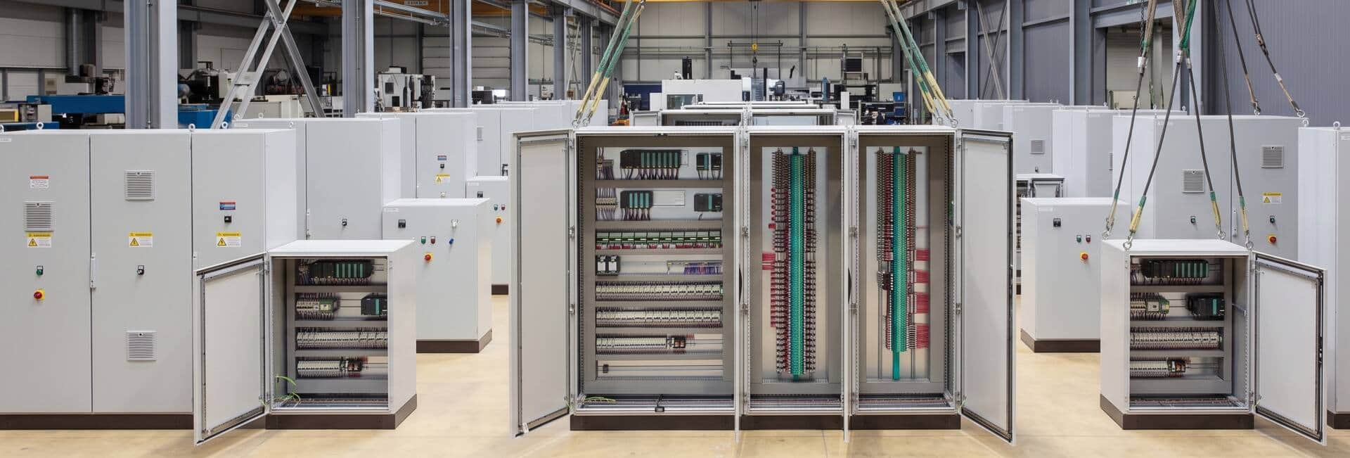 Row of control panels under build, doors open showing wired PLC racks and terminal strips